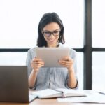 young-girl-holding-tablet-and-using-laptop-at-offi-UF2UDK6-800x800-1-1